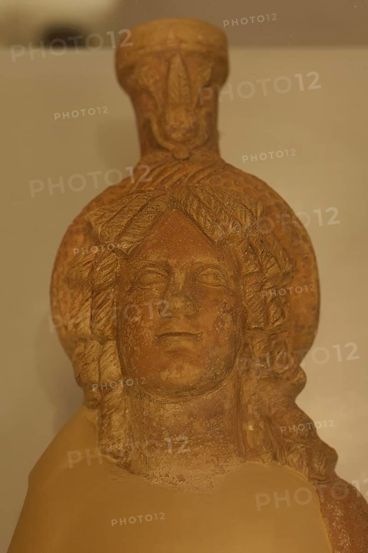 Ancient stone figurine head with elaborate hairstyle, placed on an exhibition shelf, sun disc, Archaeological Museum, Kos Town, Kos, Dodecanese, Greek Islands, Greece