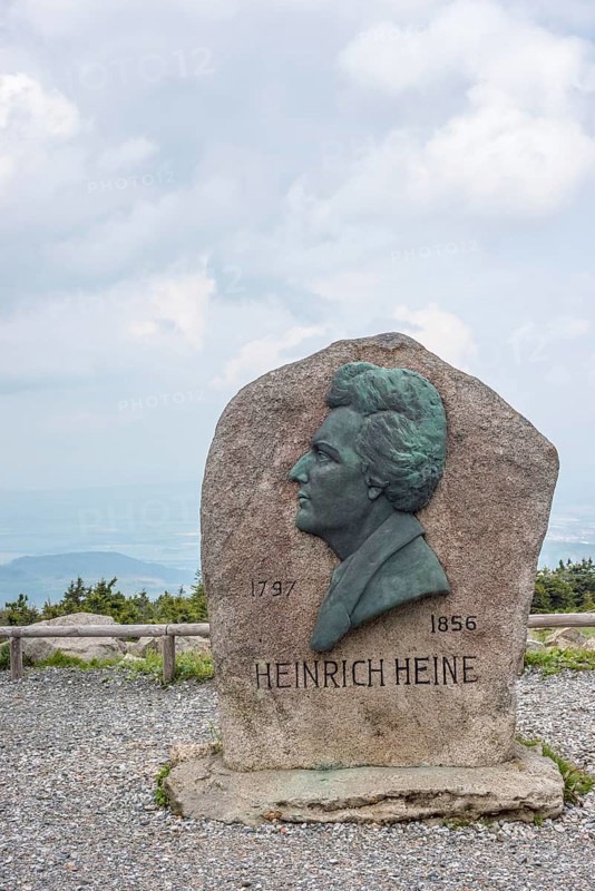 Heinrich Heine memorial, Heine memorial on the summit of the Brocken, summit plateau, granite stone with Heine plaque, portrait of the poet on bronze, inscription, year of birth, year of death, rock, forest of spruces, hazy, veiled view of the north-eastern Harz foreland, view with cloudy sky, Brocken, Harz National Park, Harz, Saxony-Anhalt, Germany