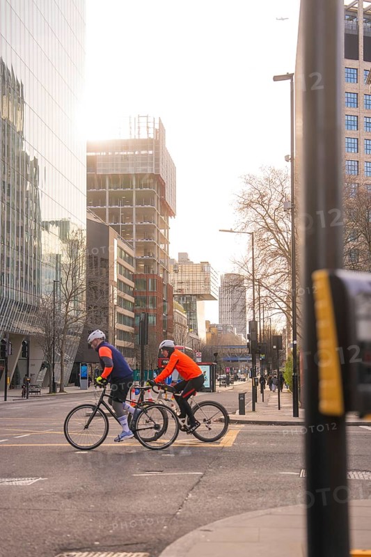 Two cyclists ride on an urban road, sunlight reflected on the buildings, London, United Kingdom, World