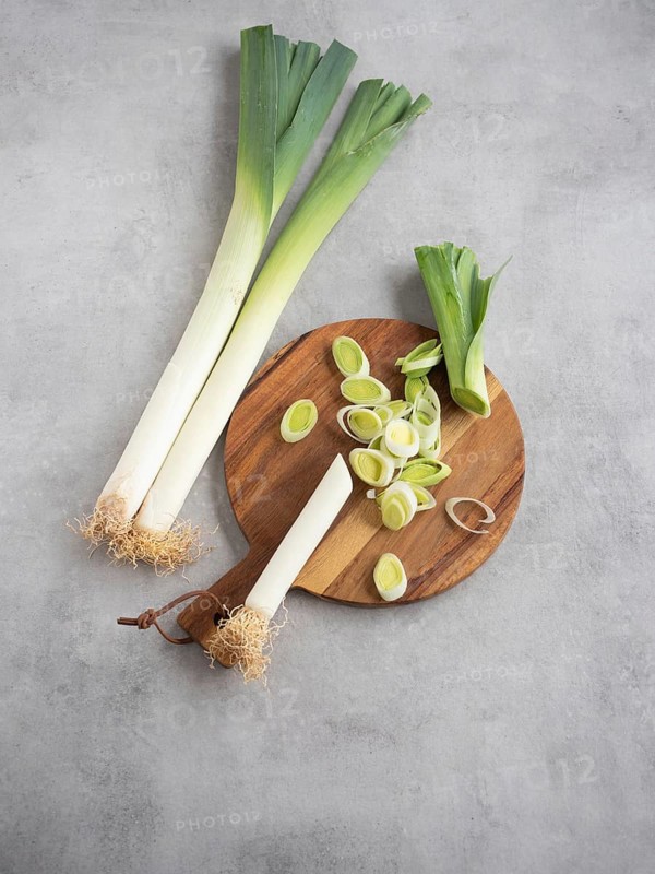 Leeks whole and cut into rings on a round cutting board