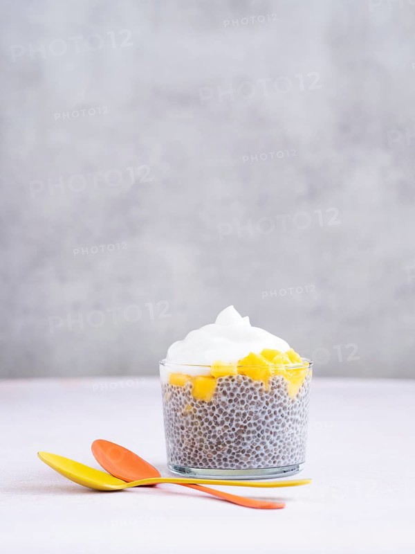 Chia seed pudding topped with diced mango and whipped cream, served with colorful spoons on a light background