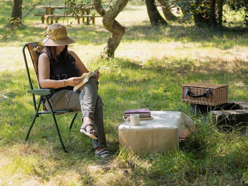 Woman enjoying a peaceful afternoon reading a book in a folding chair under a tree