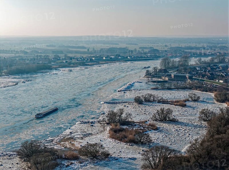 On a cold winter day, a barge sails downstream on the Elbe near Hamburg when there is slight ice. The foothills of the Elbe are icy in the flooded area. Kirchwerder, Hamburg, Germany