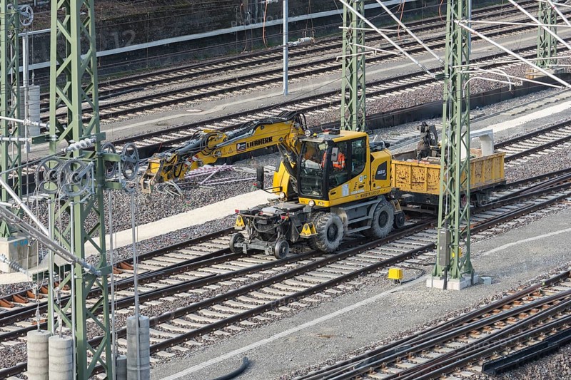 A yellow rail vehicle on a railway line surrounded by construction site equipment, Untertürkheim parking station, Stuttgart, Baden-Württemberg, Germany