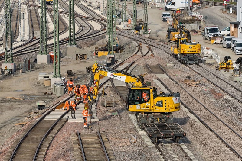 Track construction on a construction site with groups of construction workers and a yellow excavator, Untertürkheim parking station, Stuttgart, Baden-Württemberg, Germany