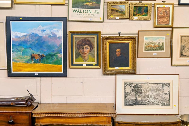 Various lots of pictures and paintings hanging on wall at auction house, UK