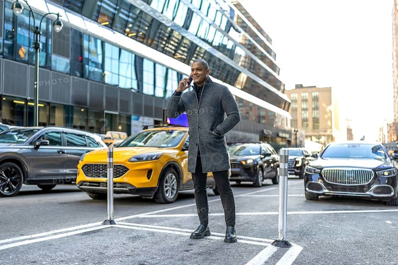 Man standing on a new york city street, making a phone call while surrounded by urban traffic and modern buildings, representing communication and a dynamic lifestyle