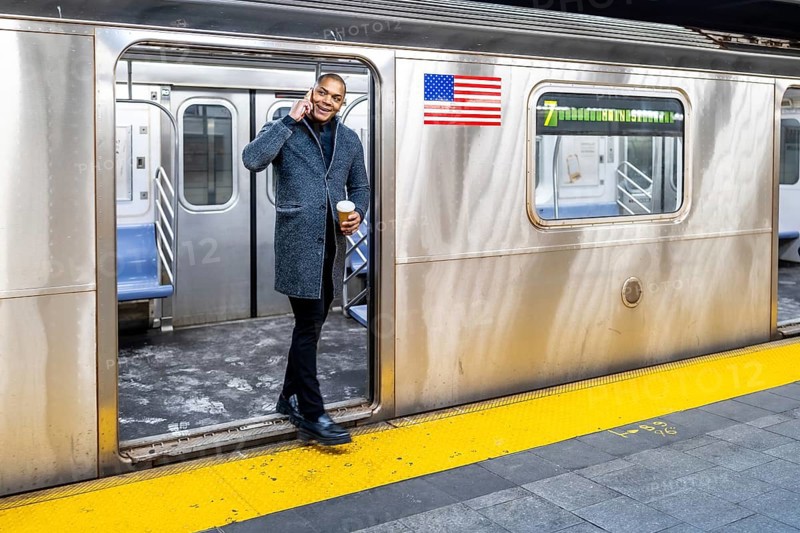 Man in smart casual attire holding coffee and talking on his mobile phone as he steps off a crowded manhattan subway onto the platform during a busy commute