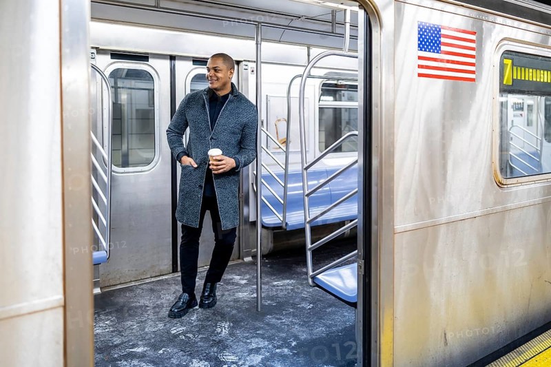 Young businessman standing on a subway car with a coffee cup, looking out through the open door, representing urban commute, travel, and daily city life in new york