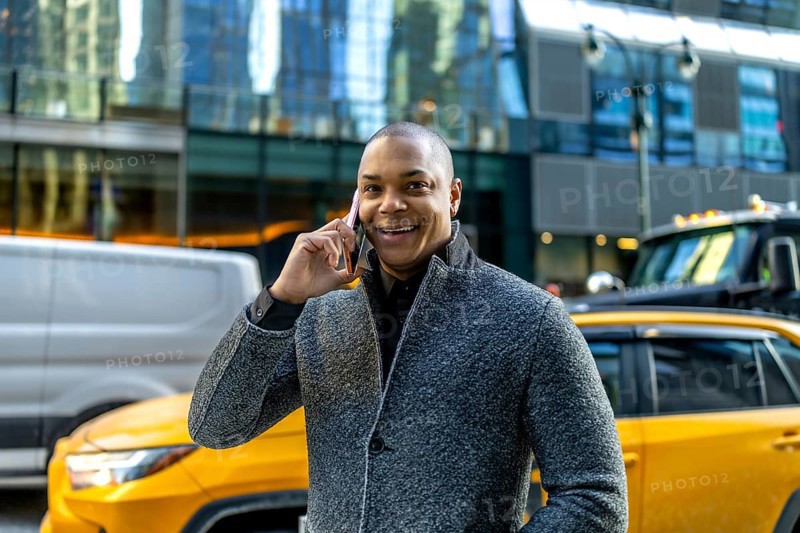 Smiling businessman making a phone call, standing on a busy street in manhattan with cars and modern office buildings in the background, representing communication and urban business