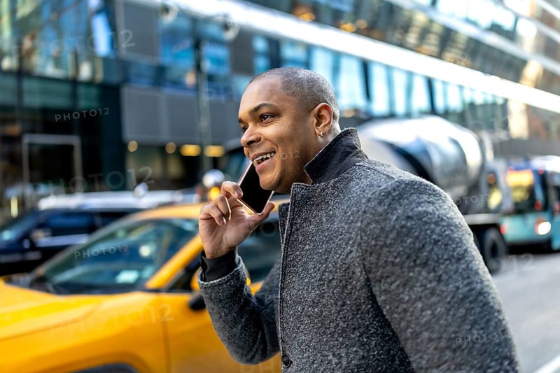 Young black businessman is walking on a city street in manhattan, new york, laughing while having a phone conversation, showing a modern urban lifestyle, communication, and connectivity