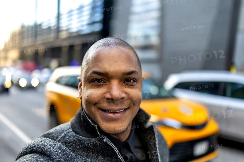 Smiling african american businessman taking a selfie on a vibrant city street, showcasing a professional and approachable demeanor amidst the bustling new york city urban background