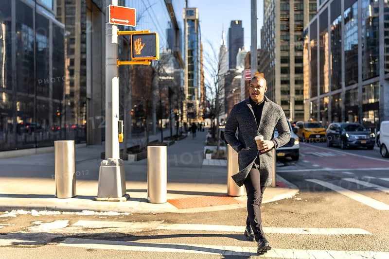 Young businessman walking confidently across a crosswalk in manhattan with a coffee cup, showcasing urban lifestyle and dynamic city energy against a backdrop of modern skyscrapers