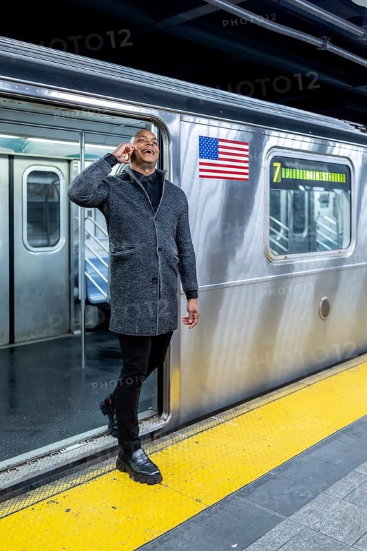 Happy professional man smiling and talking on smartphone while stepping onto a manhattan subway train, commuting through a bustling urban station for work and travel