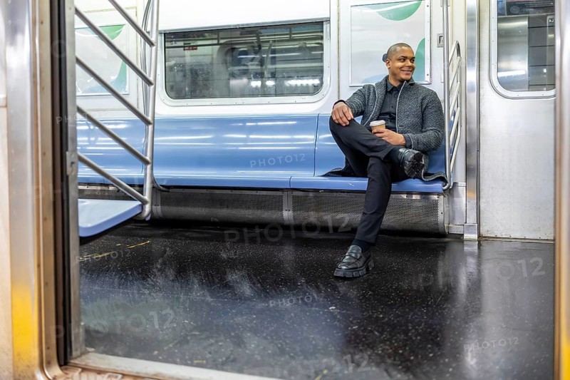 Man smiling and enjoying coffee while traveling on an empty subway car, reflecting daily commute, business lifestyle, and urban living within new york city