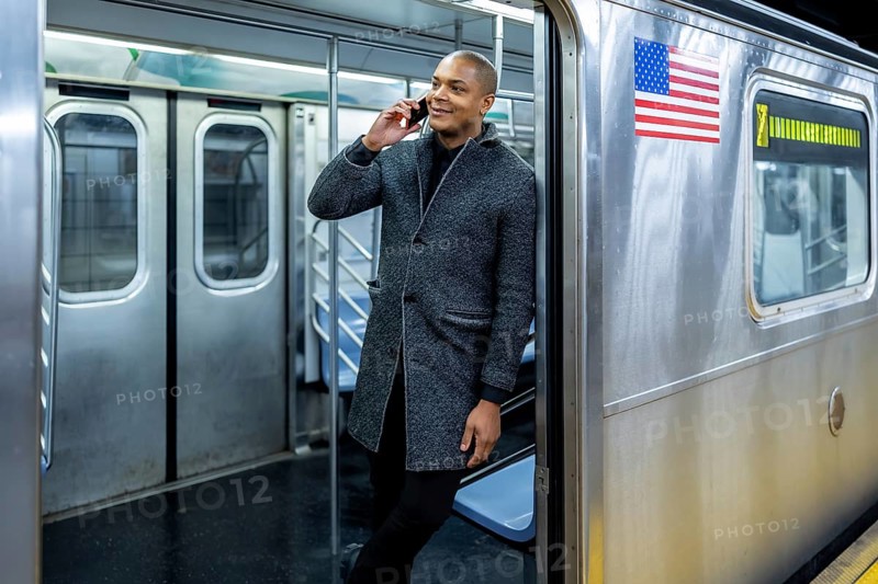 Smiling businessman traveling on a new york city subway train, talking on a mobile phone, representing urban professional life and connectivity during commute