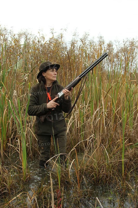 Female hunter standing in water with hunting rifle and eagerly waiting for flying ducks, Allgäu, Bavaria, Germany, Allgäu, Bavaria, Germany