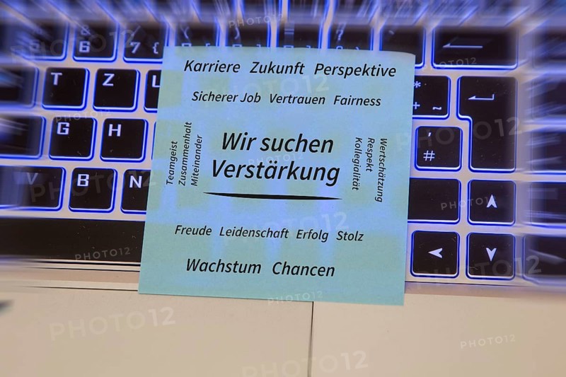 (Added) Text WE ARE LOOKING FOR REINFORCEMENT, surrounded by positive terms such as career, future, team spirit, trust, appreciation, growth and opportunities on a piece of paper lying on a laptop