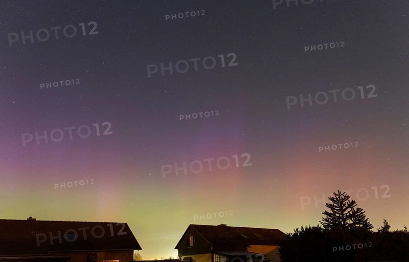 Shimmering purple and green auroras in the evening sky above residential buildings, aurora borealis, Ilsede, Lower Saxony, Germany