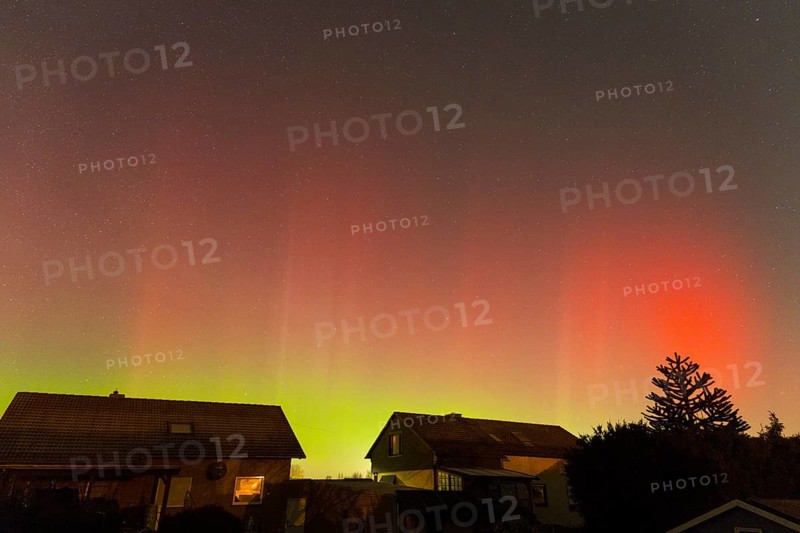 Red-green auroras illuminate the evening sky over residential buildings, aurora borealis, Ilsede, Lower Saxony, Germany