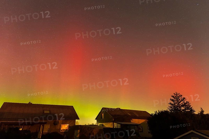 Northern lights in red and green over houses, trees and starry sky at night, aurora borealis, Ilsede, Lower Saxony, Germany