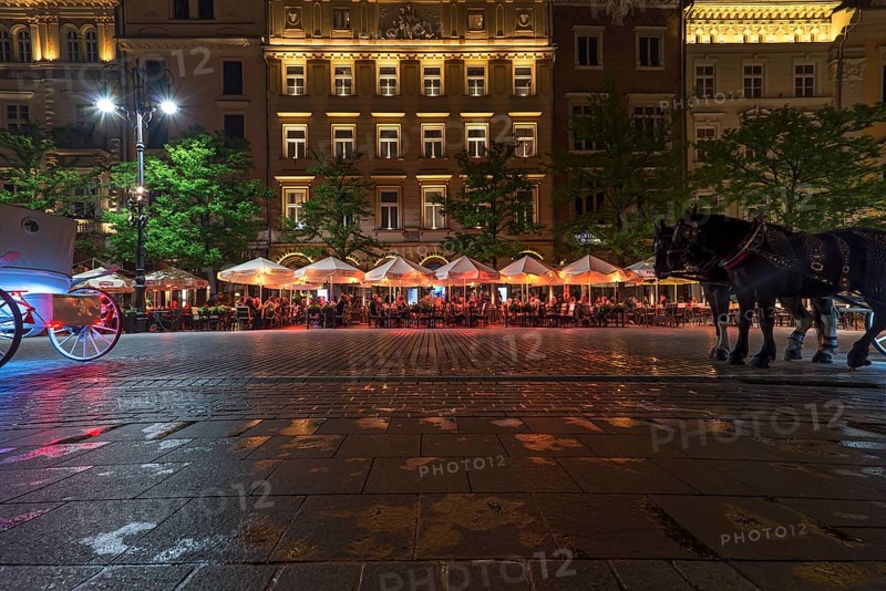 Restaurants on the market square at night, horse-drawn carriages left and right, Krakow, Poland