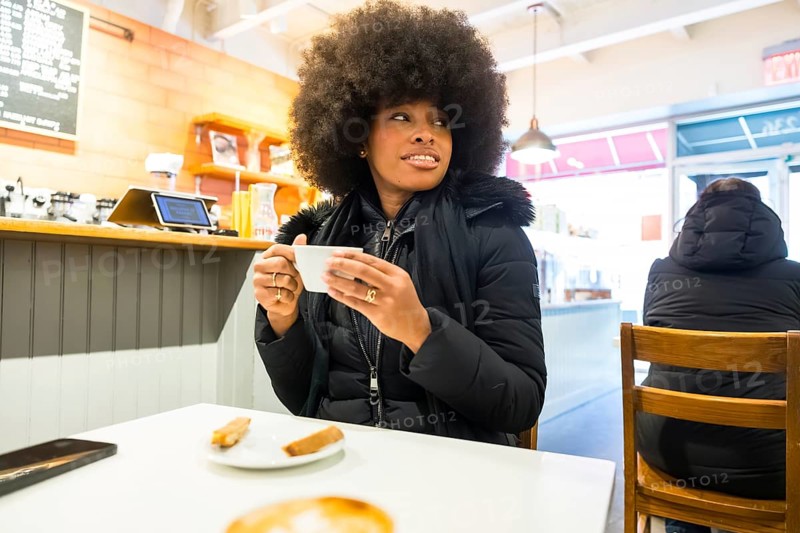 Young african american woman relaxing in a cozy manhattan coffee shop, enjoying a hot coffee during winter, embodying urban lifestyle, leisure, and social connection