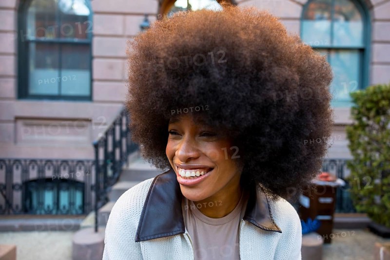 Cheerful young african american woman with a large afro hairstyle smiling genuinely, exuding joy and self acceptance while standing outdoors in a new york city neighborhood