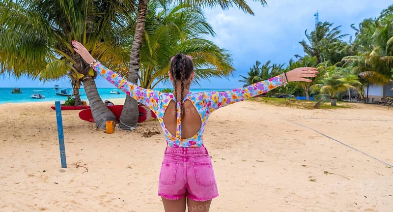 Woman with arms outstretched on white sand beach in the maldives, soaking up sunshine and turquoise sea, palms swaying, feeling carefree, relaxed and joyful on vacation