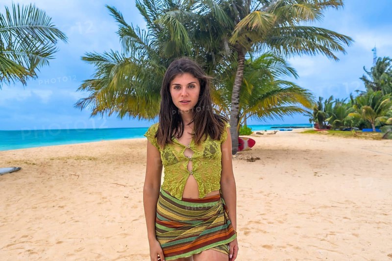 Young woman posing on a stunning tropical beach, standing in front of palm trees and turquoise ocean water, enjoying a relaxing vacation on a sunny island