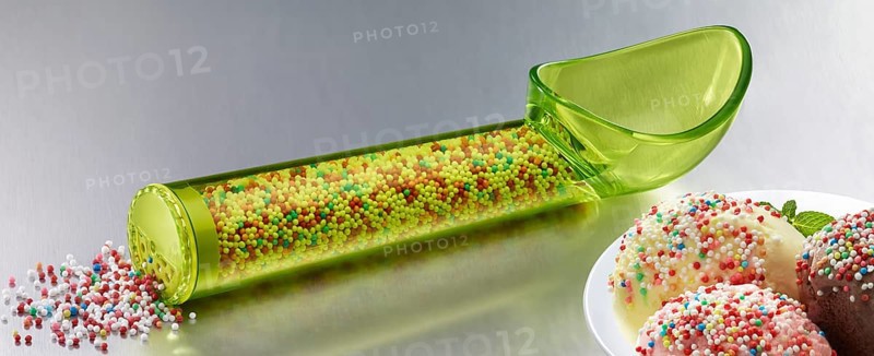 Yellow, transparent ice cream scoop filled with coloured sugar sprinkles, next to a plate with different types of ice cream, decorated with coloured sugar sprinkles