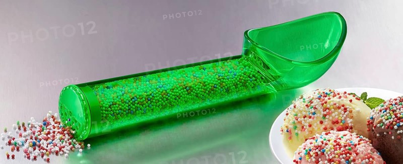 Green, transparent ice cream scoop filled with coloured sugar sprinkles, next to plates with different types of ice cream, decorated with coloured sugar sprinkles