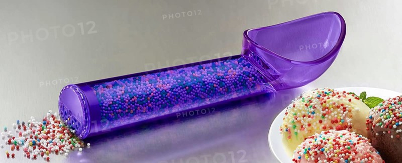 Purple, transparent ice cream scoop filled with coloured sugar sprinkles, next to plates with different types of ice cream, decorated with coloured sugar sprinkles