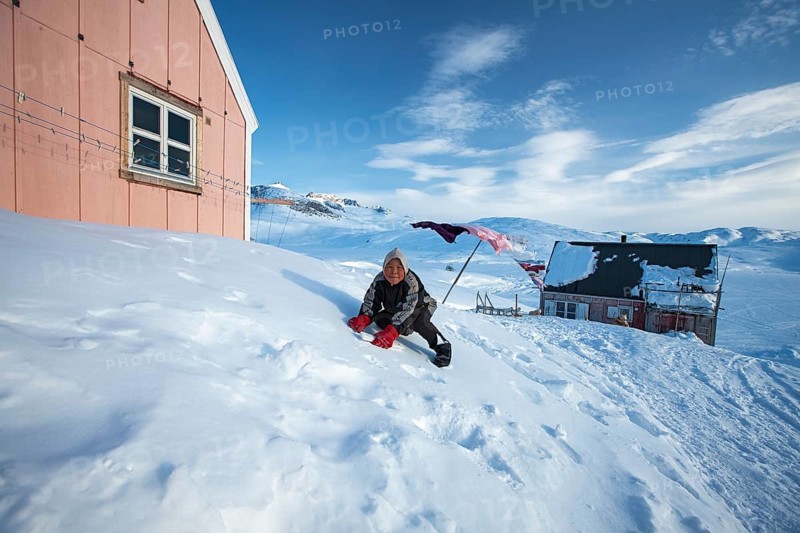 A child playing in the snow in Tiniteqilaaq. Tiniteqilaaq is one of the five settlements in the area around Ammassalik Island, located in the Sermersooq municipality on Ikasativaq Fjord, north of Ammassalik Island and facing Sermilik, Greenland, North America