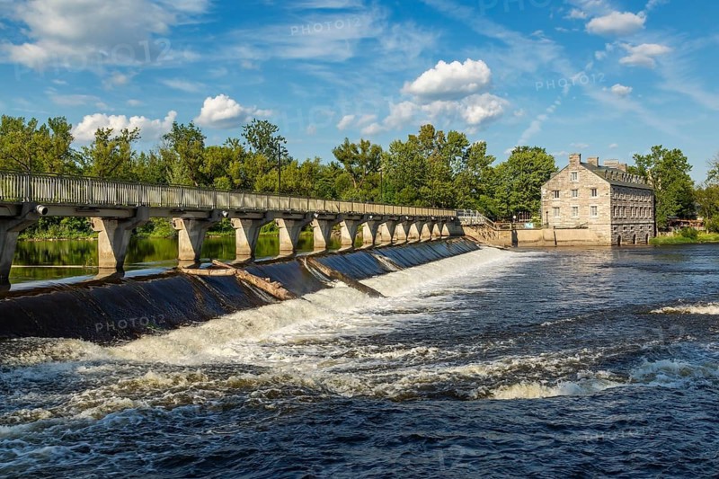 Moulin Neuf water flow control dam and walkway over Des Mille-Iles river plus New Mill on Ile des Moulins in summer, Old Terrebonne, Quebec, Canada