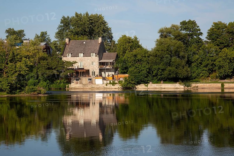19th century multistory old cut stone home with weathered cedar shingles roof and backyard built on edge of Des Mille-Iles River in summer, Terrebonne, Quebec, Canada