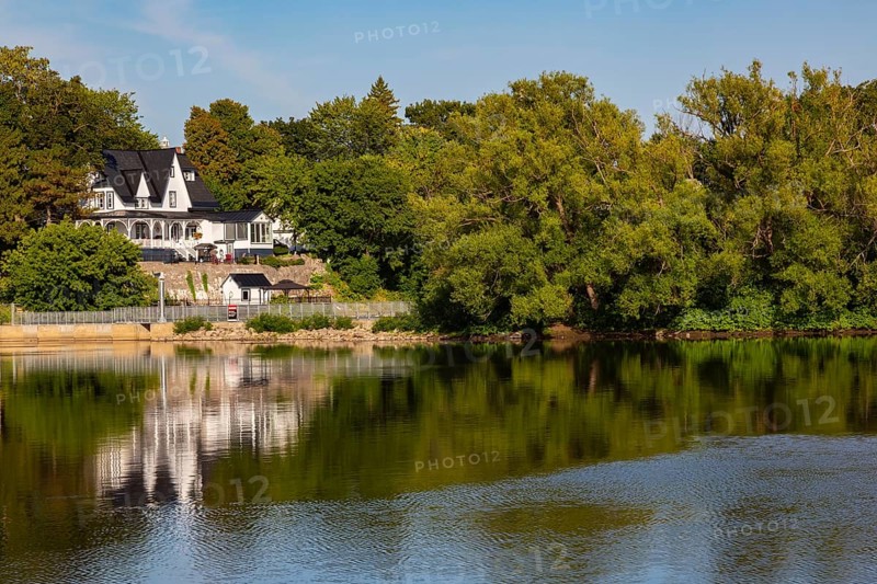 19th century multistory old white clapboard home with black rooftops and backyard built on edge of Des Mille-Iles River in summer, Terrebonne, Quebec, Canada