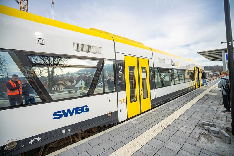 A yellow and white train is parked at a platform, passengers are waiting next to it, the Hermann Hessebahn, Calw, Germany