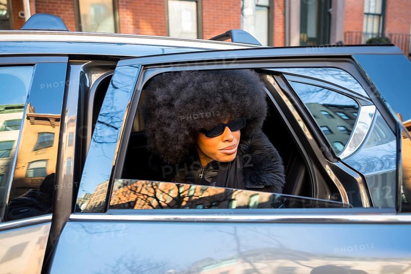 Elegant black woman wearing large sunglasses and an afro hairstyle, looking out of a car window while arriving in manhattan, new york city, capturing urban fashion and city life