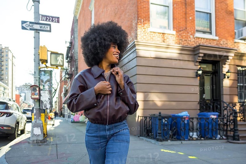 Young black woman with an afro hairstyle smiling while walking along a vibrant w 22nd street sidewalk in chelsea, new york city, enjoying urban travel and lifestyle
