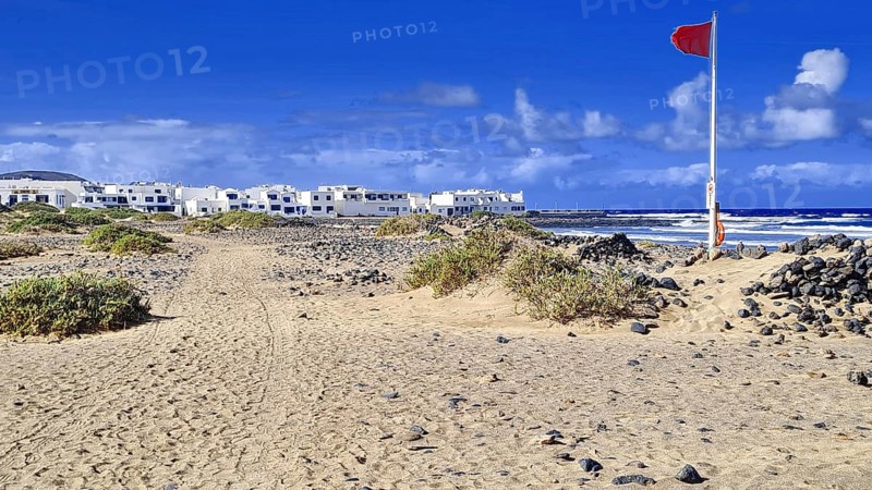 Red flag coast and adjacent village under clear skies, Caleta de Famara Lanzarote
