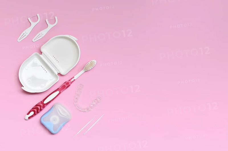 Top view of dental clear aligners, toothbrush, toothpicks and floss on pink background with copy space