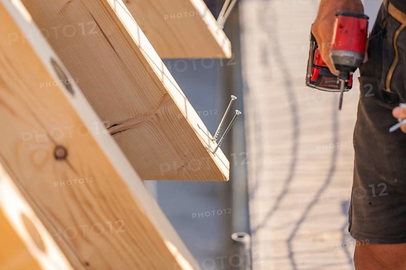 Worker holding drill next to wooden board with screws already screwed in, carpentry, new building, Stuttgart, Germany