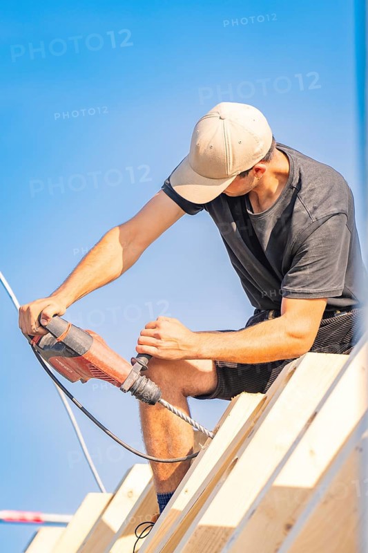 Construction worker working with a drill on a roof in sunny weather, carpentry, new building, Stuttgart, Germany
