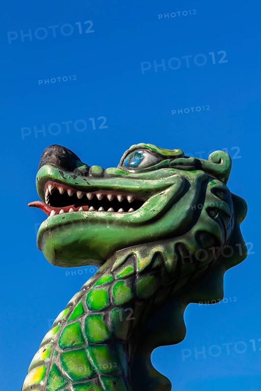 Green dragon with big teeth and long red tongue against blue sky background, Fun Show traveling amusement ride park, Old Port of Montreal, Quebec, Canada