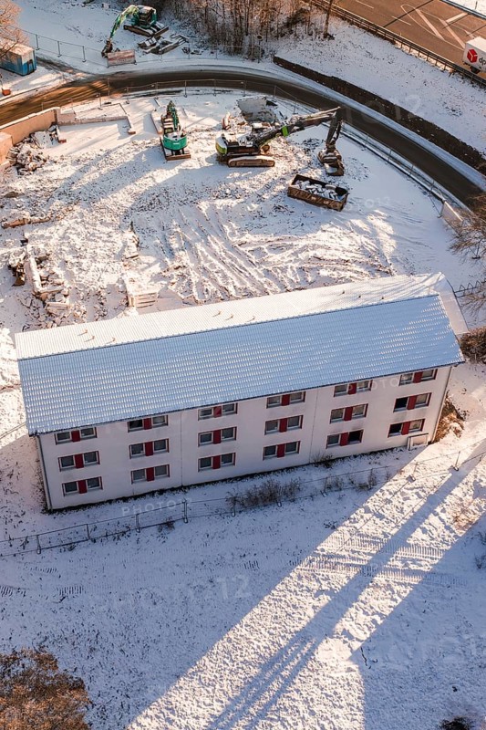Construction area in snow with construction equipment and a large white building, Nagold, Calw district, Black Forest, Germany