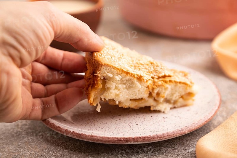 Apple Charlotte cake with hand on brown concrete background and orange linen textile, cup of milk, side view, close up, selective focus