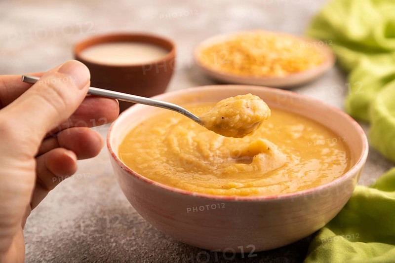 Pea cream soup, Puree, porridge in ceramic bowl with hand on brown concrete background and green linen textile. Diet, healthy eating concept. side view, close up, minimalism, selective focus