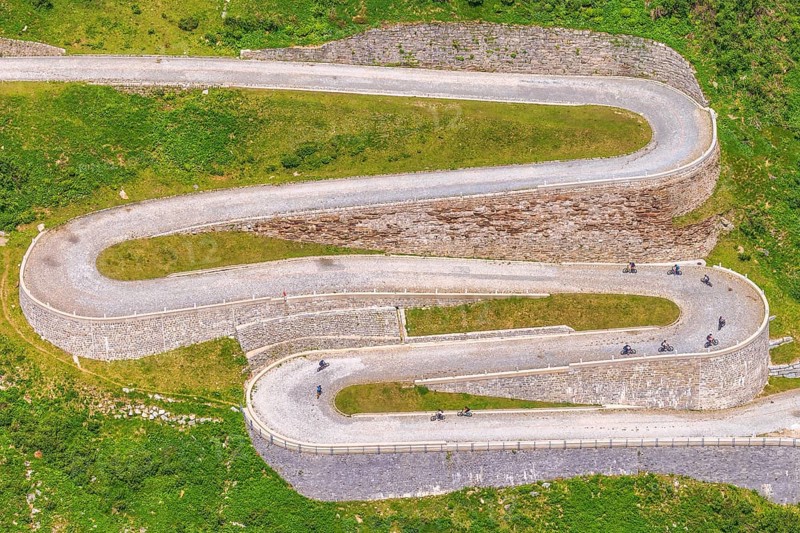 On a summer day, tourists cycle along the winding curves of Tremola Pass, Gotthard Massif, Ticino Canton, Switzerland