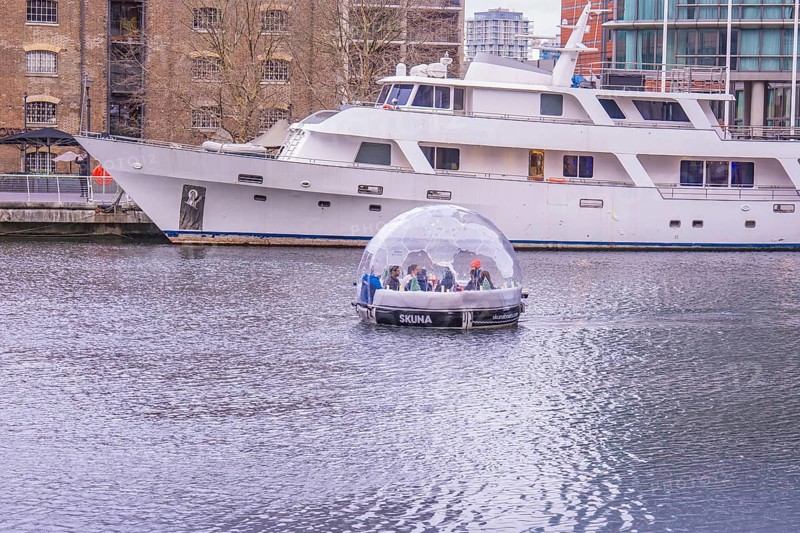 A boat with a glass dome on a body of water next to a large yacht in the harbor, London, England, Great Britain
